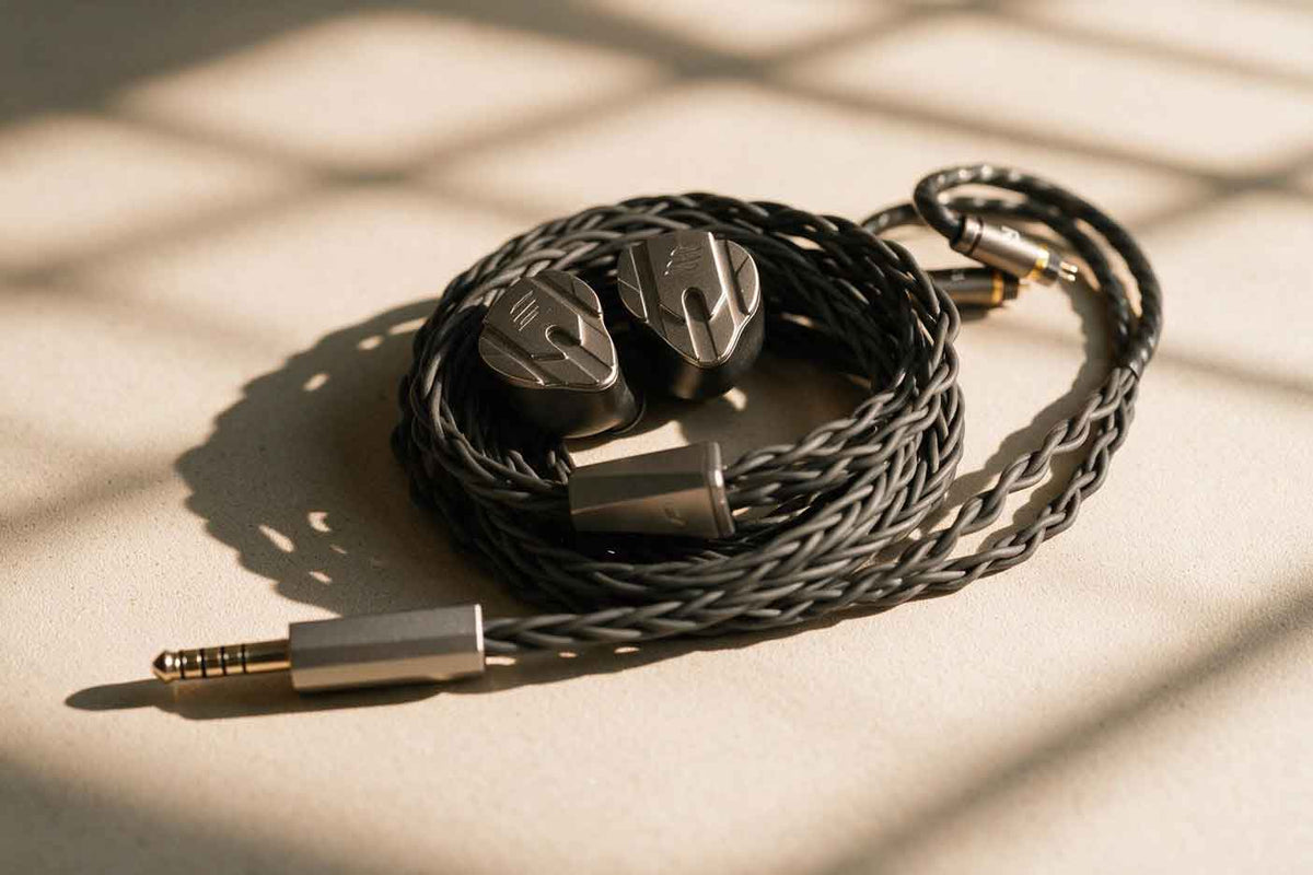 Metal in-ear monitor earpieces with faceted faceplates and braided cables resting on a dark surface in soft side lighting.